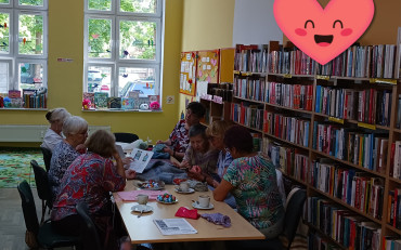 Panie siedzą przy stole i robią na drutach