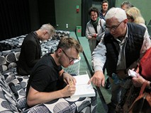 Piotr Tarczyński i Jacek Dehnel składają autografy w swoich książkach. Po prawej stronie zdjęcia wid