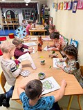 Dzieci siedzą przy stolikach i wykonują pracę plastyczną