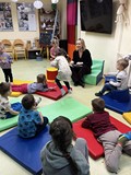 Dzieci siedzą na kolorowych pufach i słuchają bajki czytanej przez bibliotekarkę