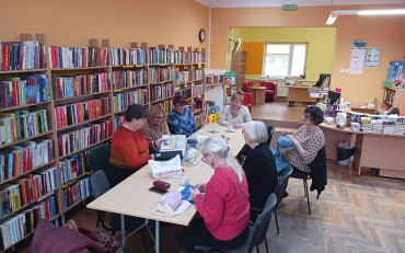 Panie siedzą przy stole, robią na drutach, rozmawiają