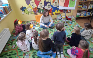 Dzieci wraz z bibliotekarką siedzą na kolorowym dywanie