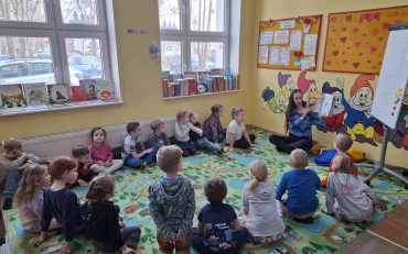 Bibliotekarka czyta dzieciom książkę, dzieci siedzą w kole