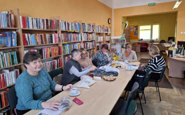 Panie siedzą przy stole, robią na drutach i rozmawiają