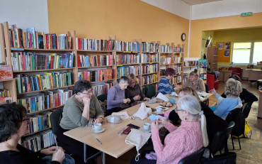 Panie siedzą przy stole, robią na drutach, rozmawiają