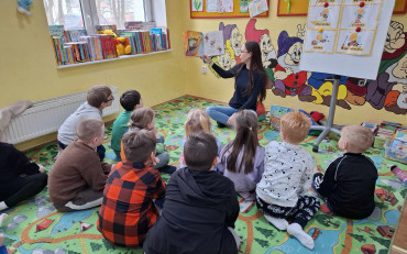 Bibliotekarka razem z dziećmi siedzi na dywanie i czyta książkę
