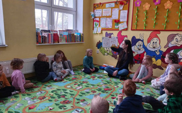 Bibliotekarka czyta dzieciom książkę, dzieci siedzą w kole na dywanie