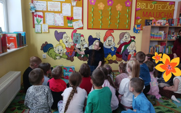 Bibliotekarka czyta dzieciom książkę, dzieci siedzą w kole