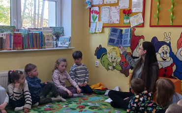 Bibliotekarka czyta dzieciom książkę, dzieci siedzą w kole na dywanie