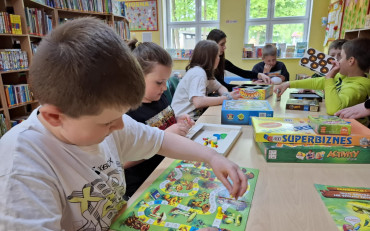 dzieci siedzą przy stole i grają  w gry planszowe
