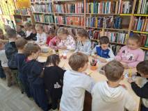 Dzieci stoją przy stolikach i wykonują pracę plastyczną