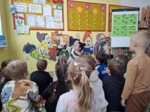 Bibliotekarka czyta dzieciom książkę, dzieci siedzą przodem do bibliotekarki