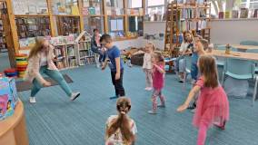 Dzieci pod kierunkiem bibliotekarza wykonują ćwiczenia gimnastyczne
