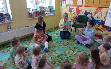 Bibliotekarka czyta dzieciom książkę, dzieci siedzą w kole