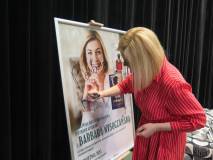 Pisarka Barbara Wysoczańska składa podpis na plakacie zapowiadającym spotkanie