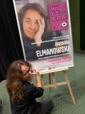 Pisarka Barbara Elmanowska podpisuje plakat promujący spotkanie autorskie