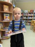 Chłopiec trzyma książeczkę, stoi na tle regału z książkami.
