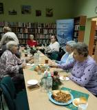 Na zdjęciu uczestnicy rozmawiają, na stole ciasto i herbata.