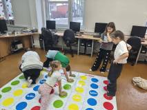Piątka dzieci gra w grę Twister, na białym polu w kolorowe kulki.