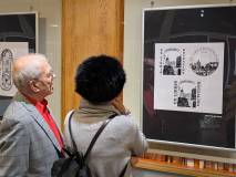 Dwoje uczestników po lewej przygląda się wiszącemu wydrukowi ekslibrisu po prawej.