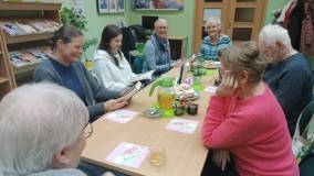 Dyskusja o książce, na stole stoi dzbanek z herbatą i talerz z faworkami.