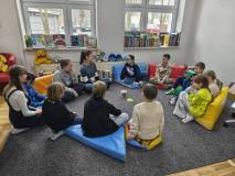 Dzieci wraz z bibliotekarką siedzą w kole i rozmawiają