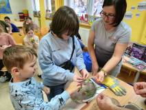 Na zdjęciu pani Kinga pomaga uczestnikom warsztatów zamrozić róże, wkładając je do miski z ciekłym a