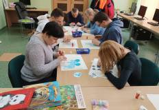 Uczestnicy wyklejają papierowe modele zwierząt.