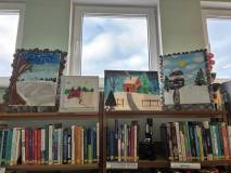 Prace plastyczne dzieci o tematyce zimowej wyeksponowane na regale w bibliotece