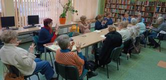 Uczestnicy spotkania ćwiczą przy stole mudry pod okiem prowadzącej.