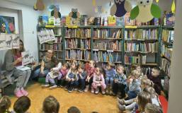 Bibliotekarka pokazuje dzieciom sylwetki dinozaurów.