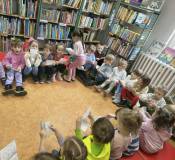 Dzieci otrzymują kolorowanki od bibliotekarki.