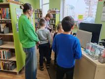 Pani Ania oprowadza grupę po bibliotece. Na zdjęciu „Elfy” ze swoją panią stoją przy biurku w wypoży