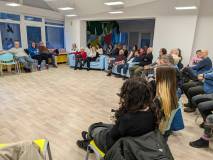 Ujęcie z perspektywy jednego z uczestników, pokazujące zgromadzoną publiczność. Ludzie siedzą w luźn