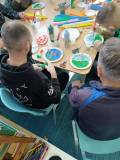 Osadzeni wykonują prace plastyczne siedząc przy stołach 