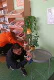 Uczestnicy wycierają regał z prasą i stolik w czytelni. 