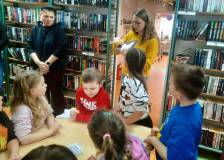 Bibliotekarka pokazuje dzieciom jak odrysować kształt motyla za pomocą pasteli.