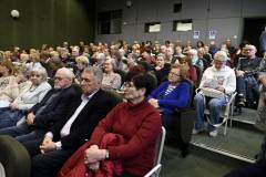 Widok na wypełnioną salę audytoryjną z perspektywy bocznej. W rzędach siedzi liczna grupa osób, głów