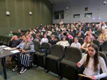 Widok na publiczność zgromadzoną w sali audytoryjnej. W rzędach siedzi liczna grupa dzieci i młodzie