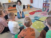 Bibliotekarka i dzieci siedzą na dywanie i rozmawiają o wiośnie.