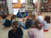 Na zdjęciu Gosia prezentuje plansze z wizerunkami dinozaurów, a siedzące na podłodze dzieci odgadują