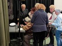 Ujęcie z boku przedstawiające moment podpisywania książek po spotkaniu. Autorka siedzi przy stole i 