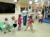 Dzieci w trakcie zabawy z balonami. Bibliotekarka trzyma wysoko hula-hop a dzieci przerzucają przez 