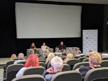 Widok z tyłu sali kinowej na scenę podczas dyskusji. Na pierwszym planie widać głowy i ramiona osób 