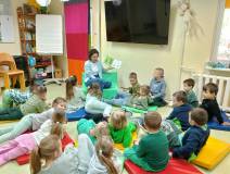 Bibliotekarka czyta dzieciom książkę. Dzieci siedzą na kolorowych materacykach.