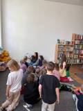 Bibliotekarka czyta książkę, a dzieci  siedzą na szarym dywanie