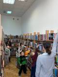 Dzieci stoją przy regale i pokazują najwyżej położne książki