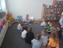 Bibliotekarka czyta dzieciom książkę, dzieci siedzą na dywanie