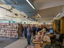Szerokie ujęcie wnętrza biblioteki publicznej. Widoczne są regały wypełnione książkami, lada bibliot