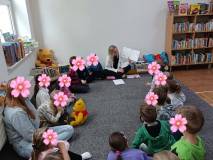 Dzieci siedzą w kole wraz z bibliotekarką, która czyta książkę